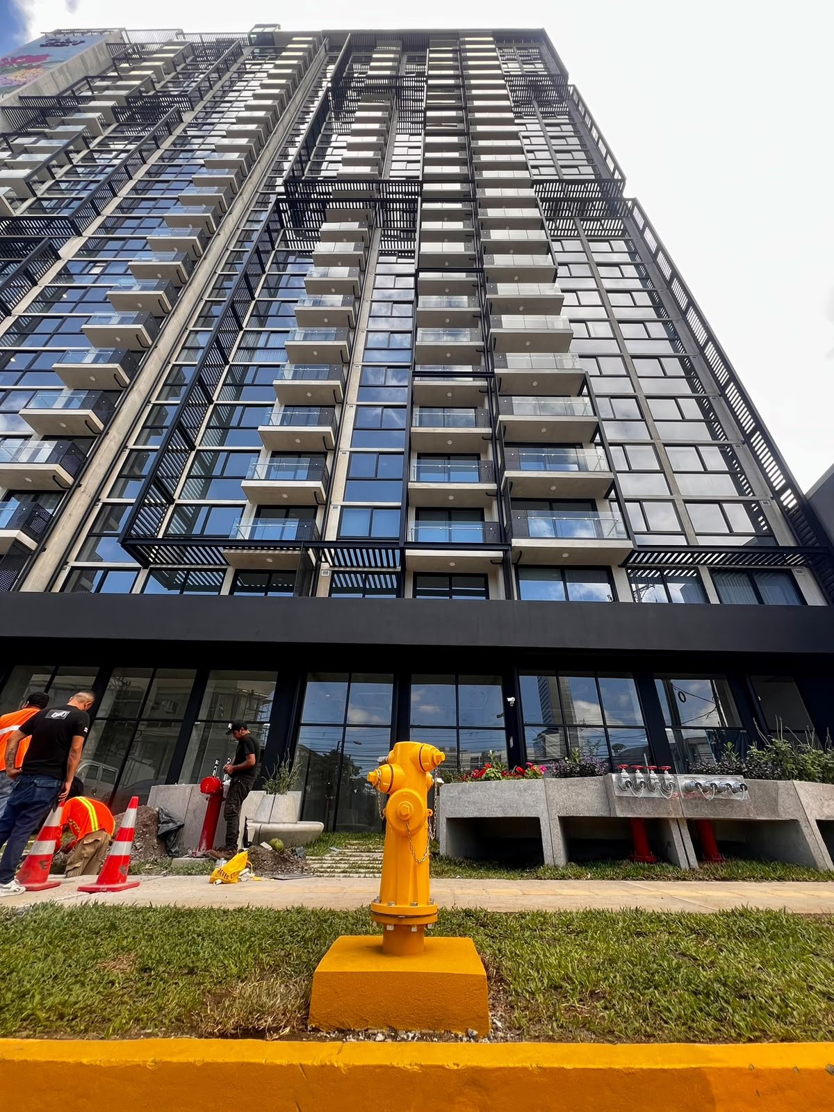 Hidrante amarillo instalado frente a un edificio, con personal de obra al fondo